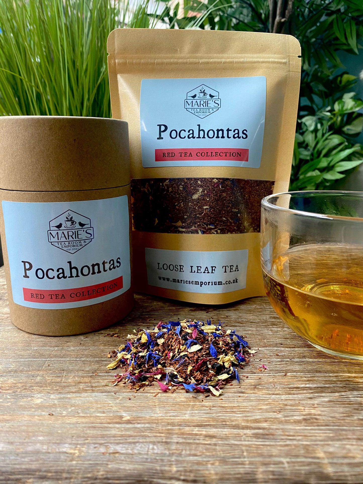 Loose leaf tea labeled "Pocahontas" from Marie's Emporium, in jar and pouch, with a glass of tea and colorful blend on a wooden surface. Relaxing, natural setting.