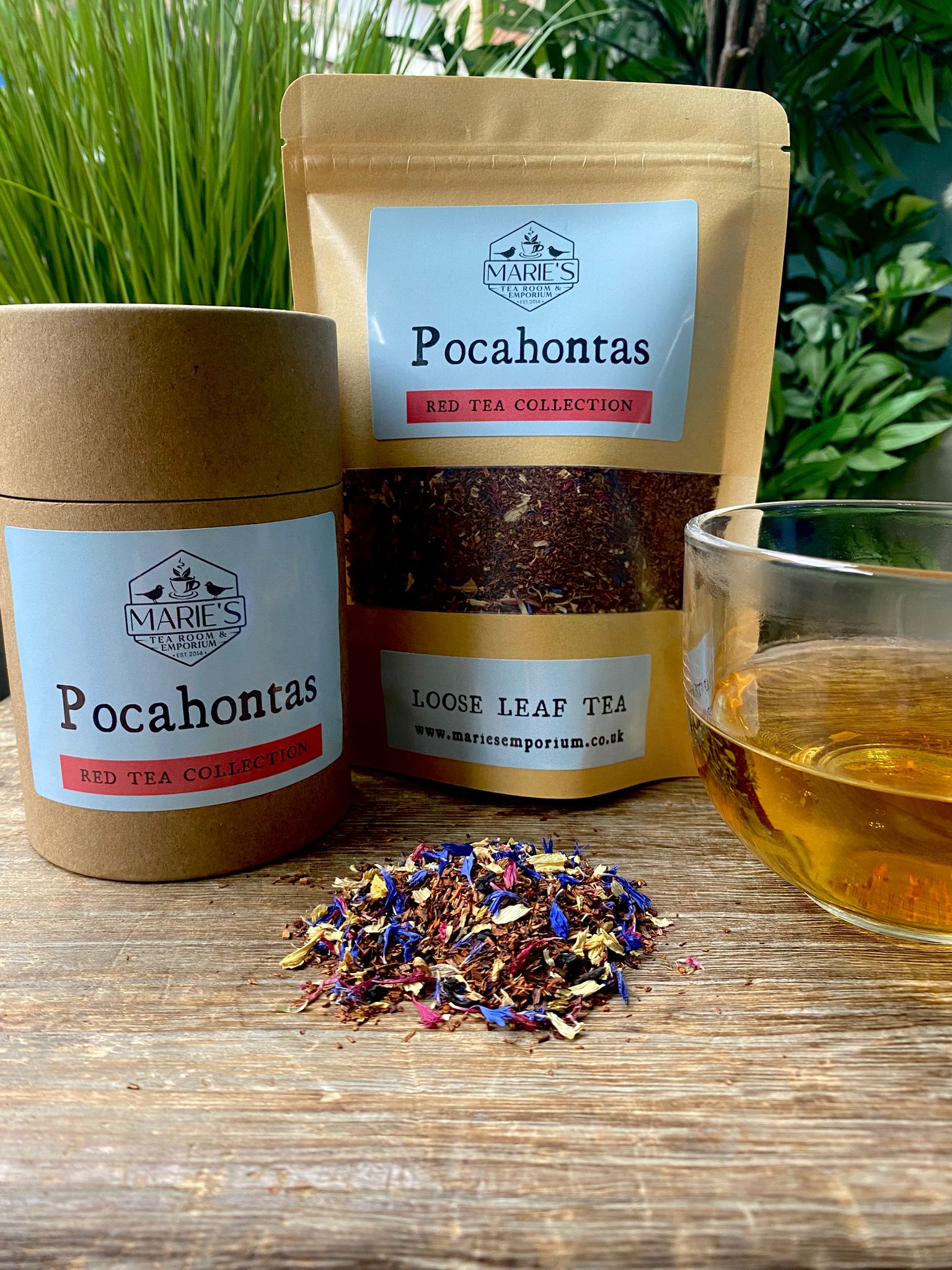 Loose leaf tea labeled "Pocahontas" from Marie's Emporium, in jar and pouch, with a glass of tea and colorful blend on a wooden surface. Relaxing, natural setting.