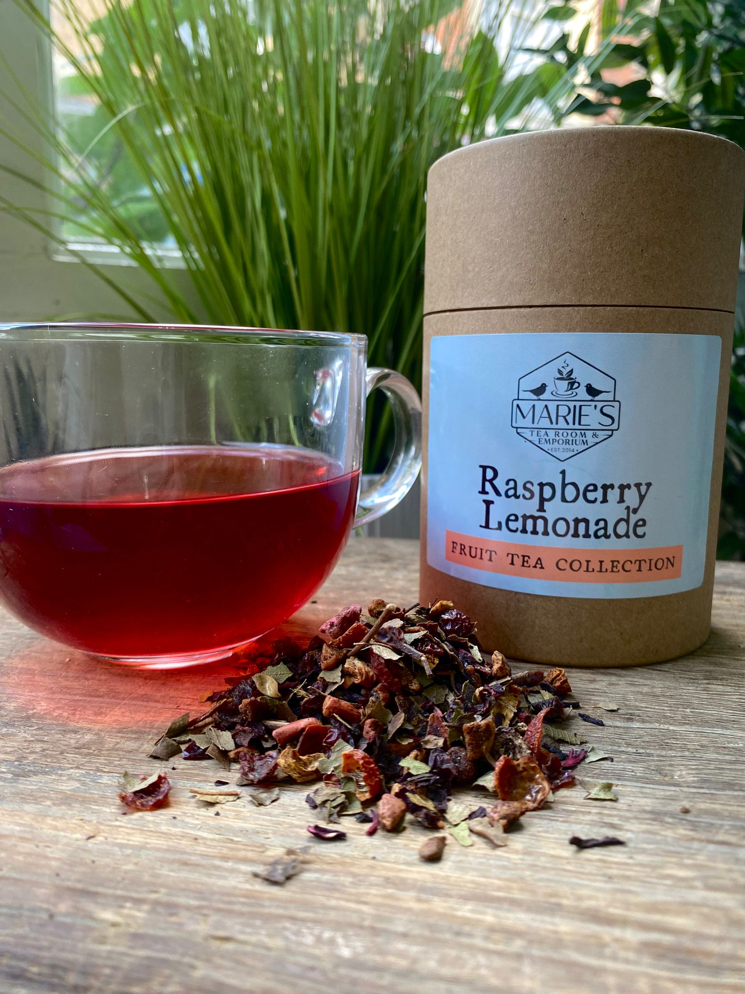 maries raspberry lemonade Tea packaging with a glass of tea and dried tea leaves on a wooden surface.