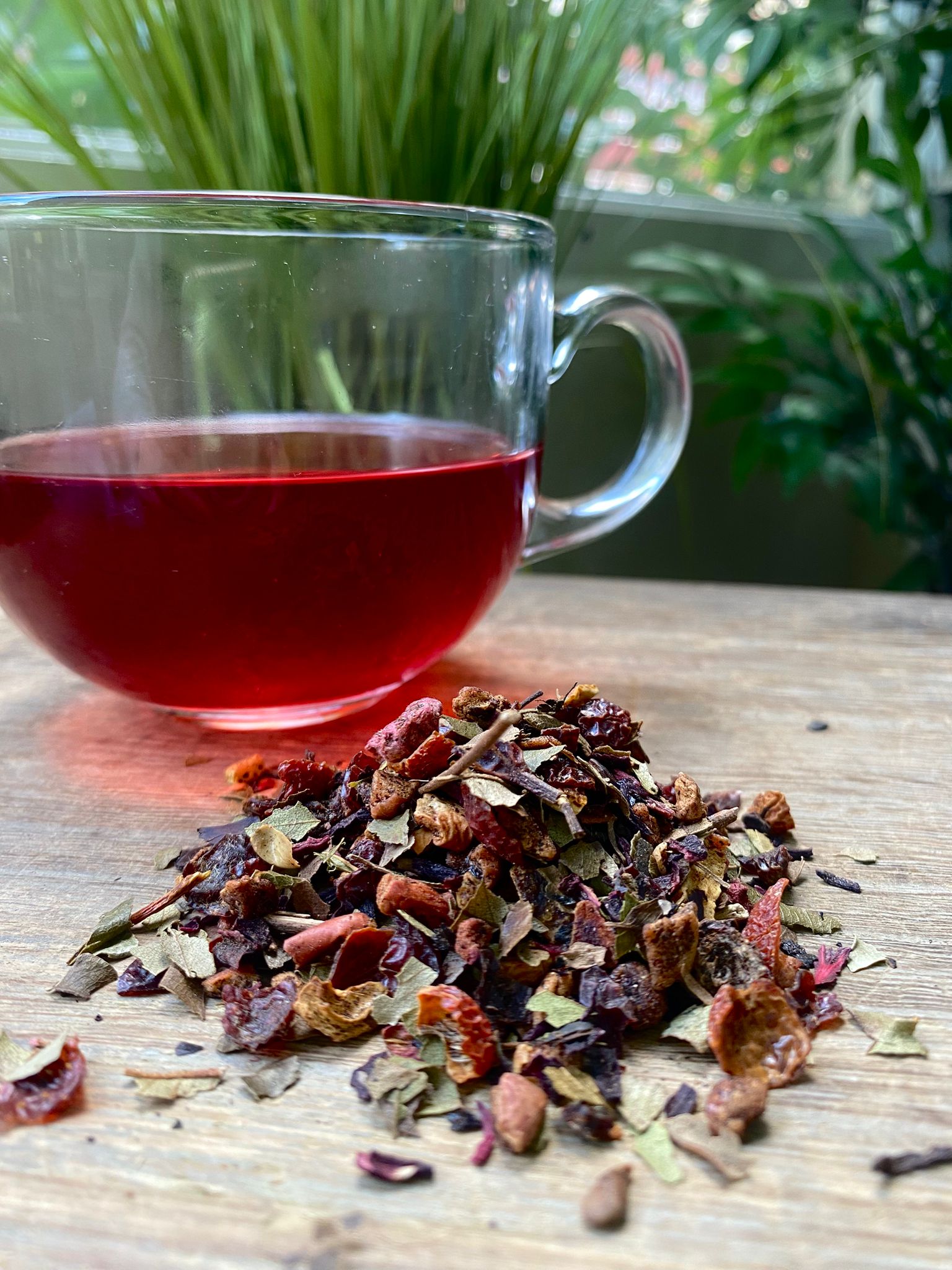Marie’s Raspberry Lemonade loose leaf tea with brewed fruit tea in a clear glass mug and loose tea leaves on a wooden surface