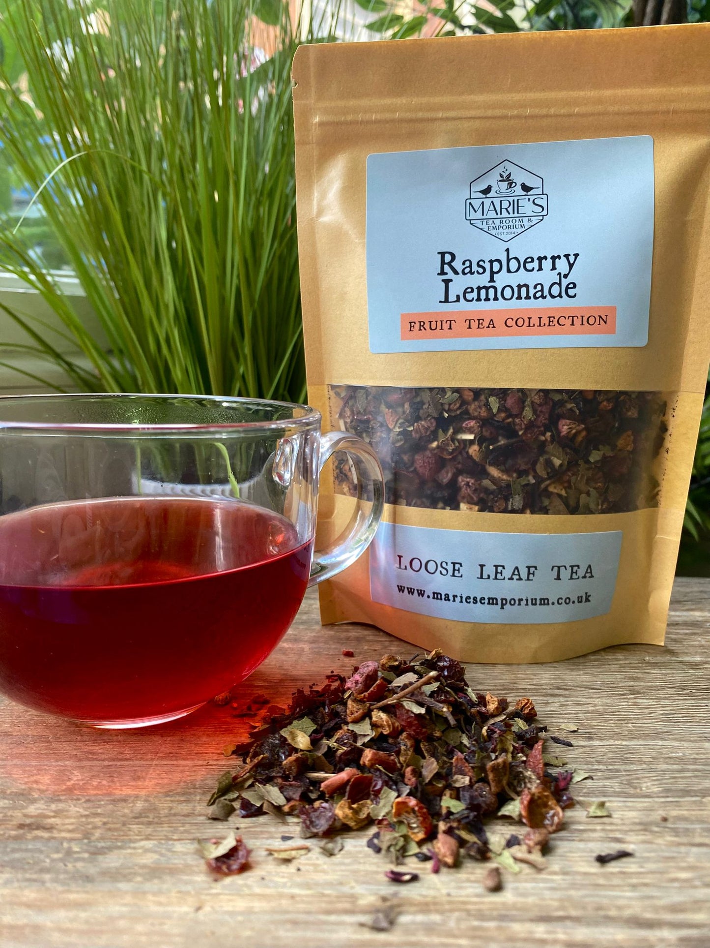 maries Raspberry Lemonade loose leaf tea package with a cup of tea and tea leaves on a wooden surface.