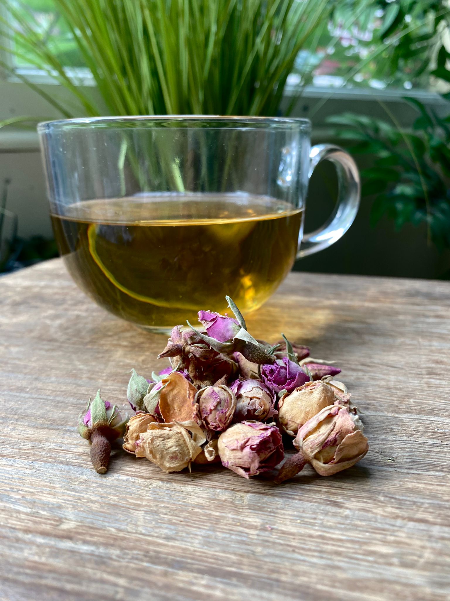 Marie’s rose bud loose leaf tea with brewed herbal tea in a clear glass mug and loose tea leaves on a wooden surface