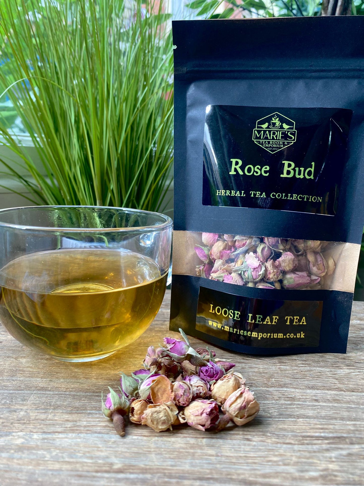 Marie's Emporium Rose Bud loose leaf tea package with a glass of tea and tea leaves on a wooden surface.