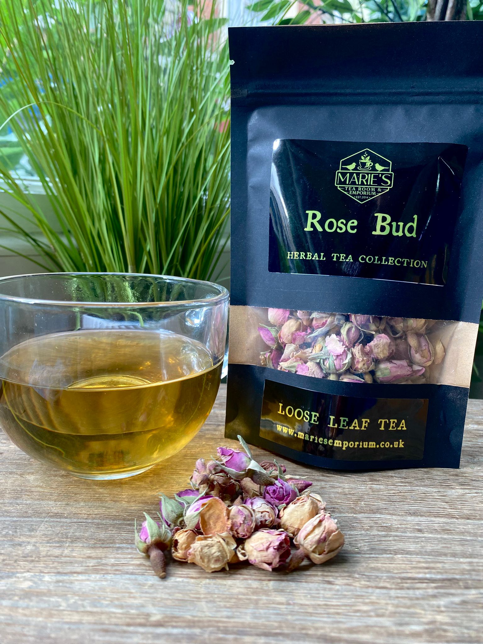 Marie's Emporium Rose Bud loose leaf tea package with a glass of tea and tea leaves on a wooden surface.