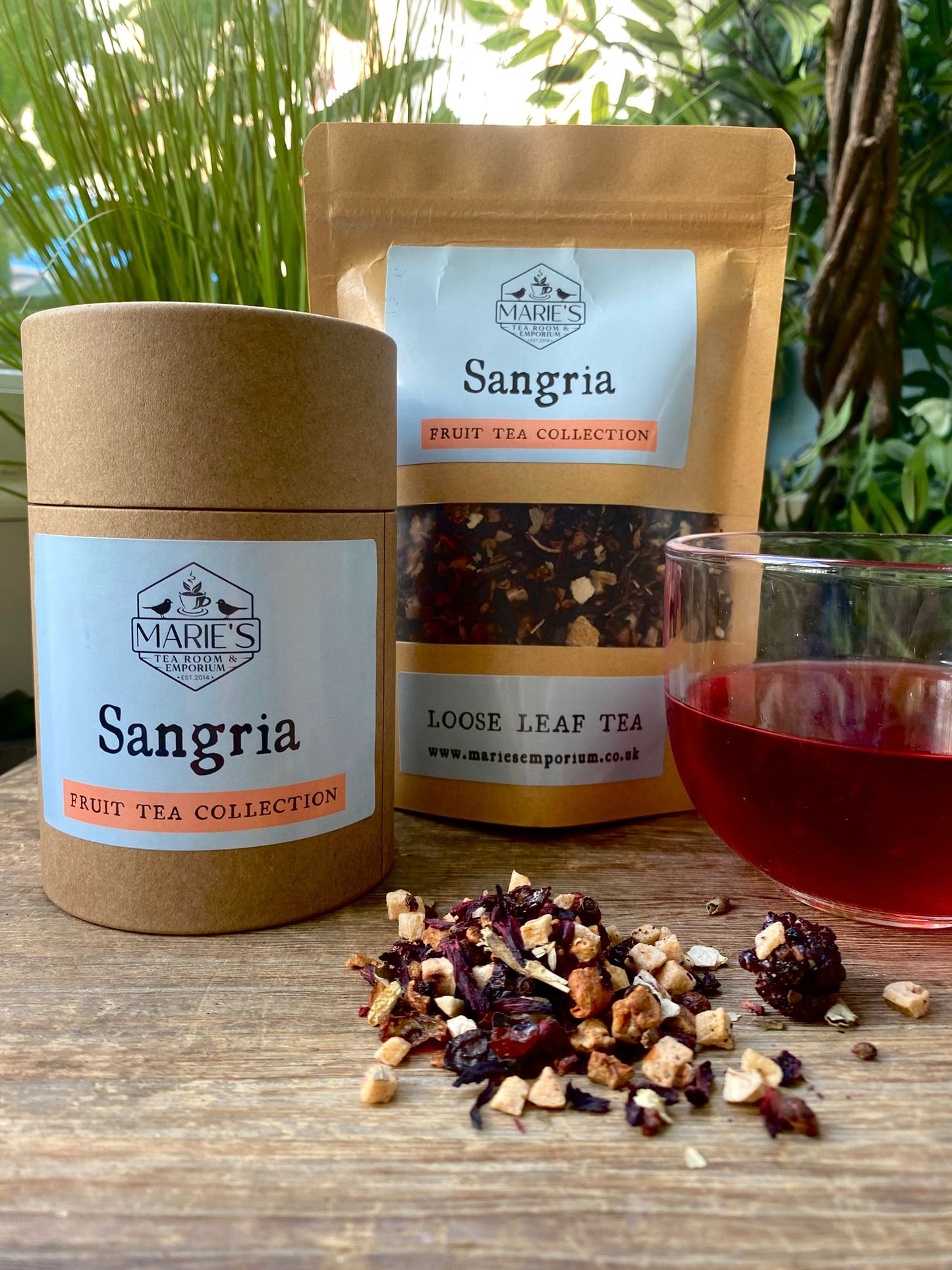Marie's Emporium Sangria loose leaf tea packaging with tea leaves and a glass of tea on a wooden surface.