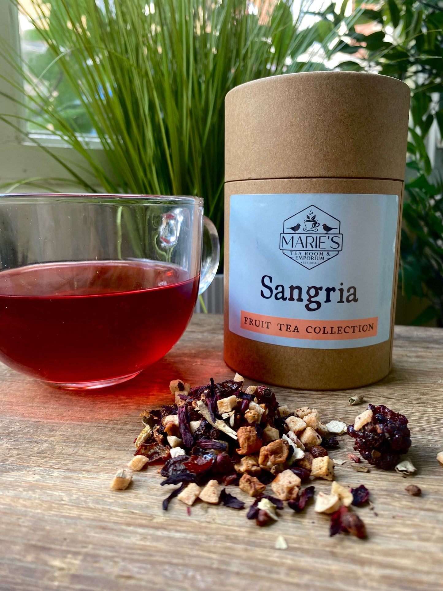 
Tea canister labeled 'Sangria' from Marie's Tea Collection with a cup of tea and tea leaves on a wooden surface.