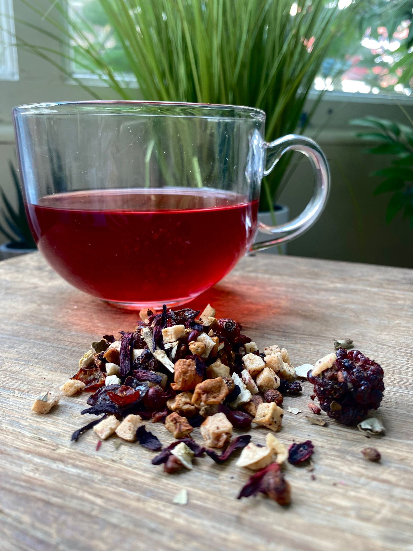 Maries Sangria loose leaf tea with brewed fruit tea in a clear glass mug and loose tea leaves on a wooden surface