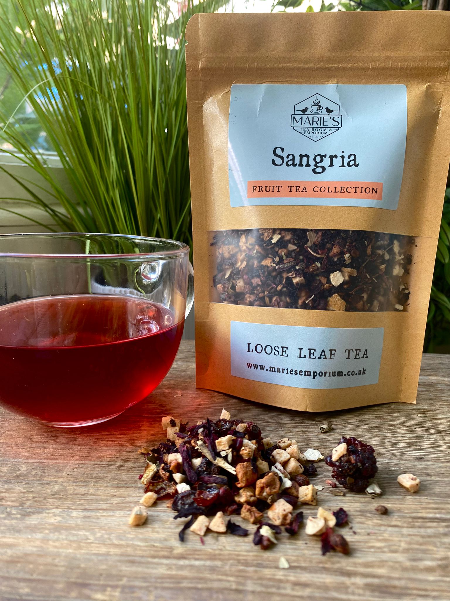 maries Sangria loose leaf tea package with a glass of tea and tea leaves on a wooden surface.
