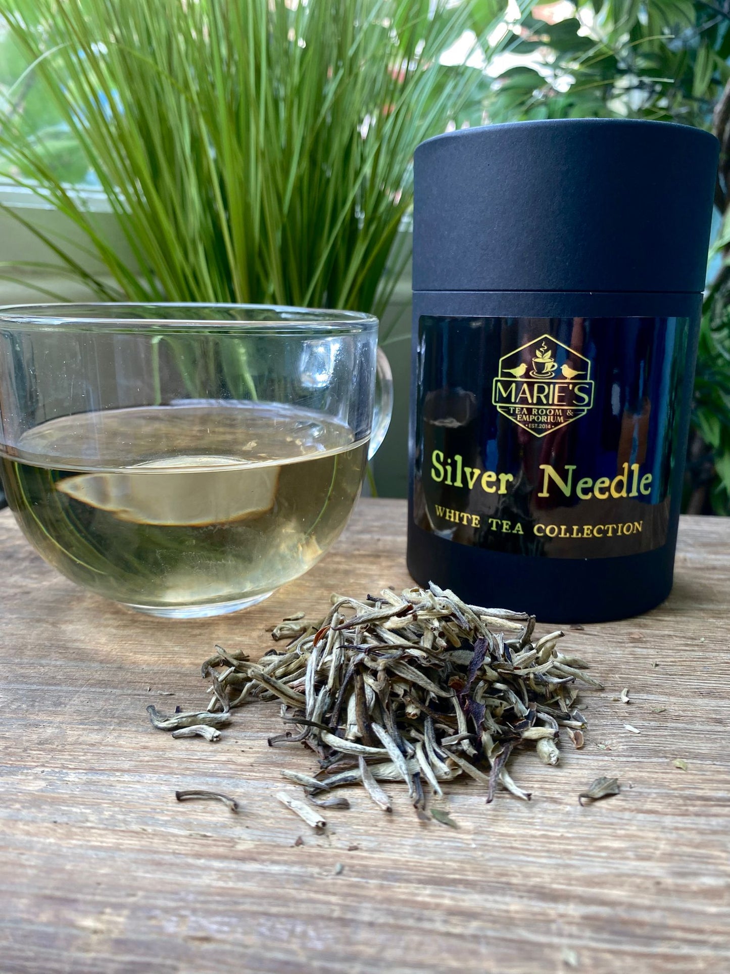 silver needle maries loose leaf Tea packaging with a glass of tea and loose tea leaves on a wooden surface.
