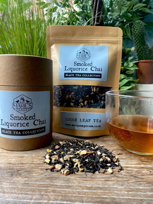 Marie's Emporium Smoked Liquorice Chai tea packaging with loose tea leaves and a glass of tea on a wooden surface.