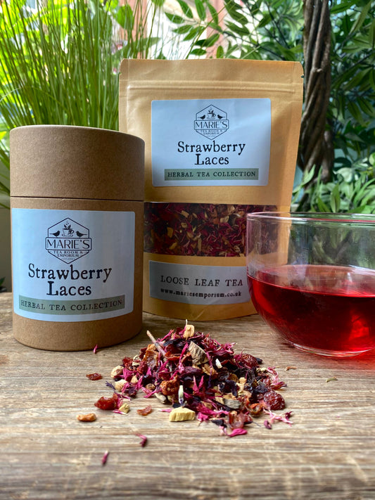 Marie's Strawberry Laces herbal tea collection with loose leaf tea, packaging, and a glass of tea on a wooden surface.