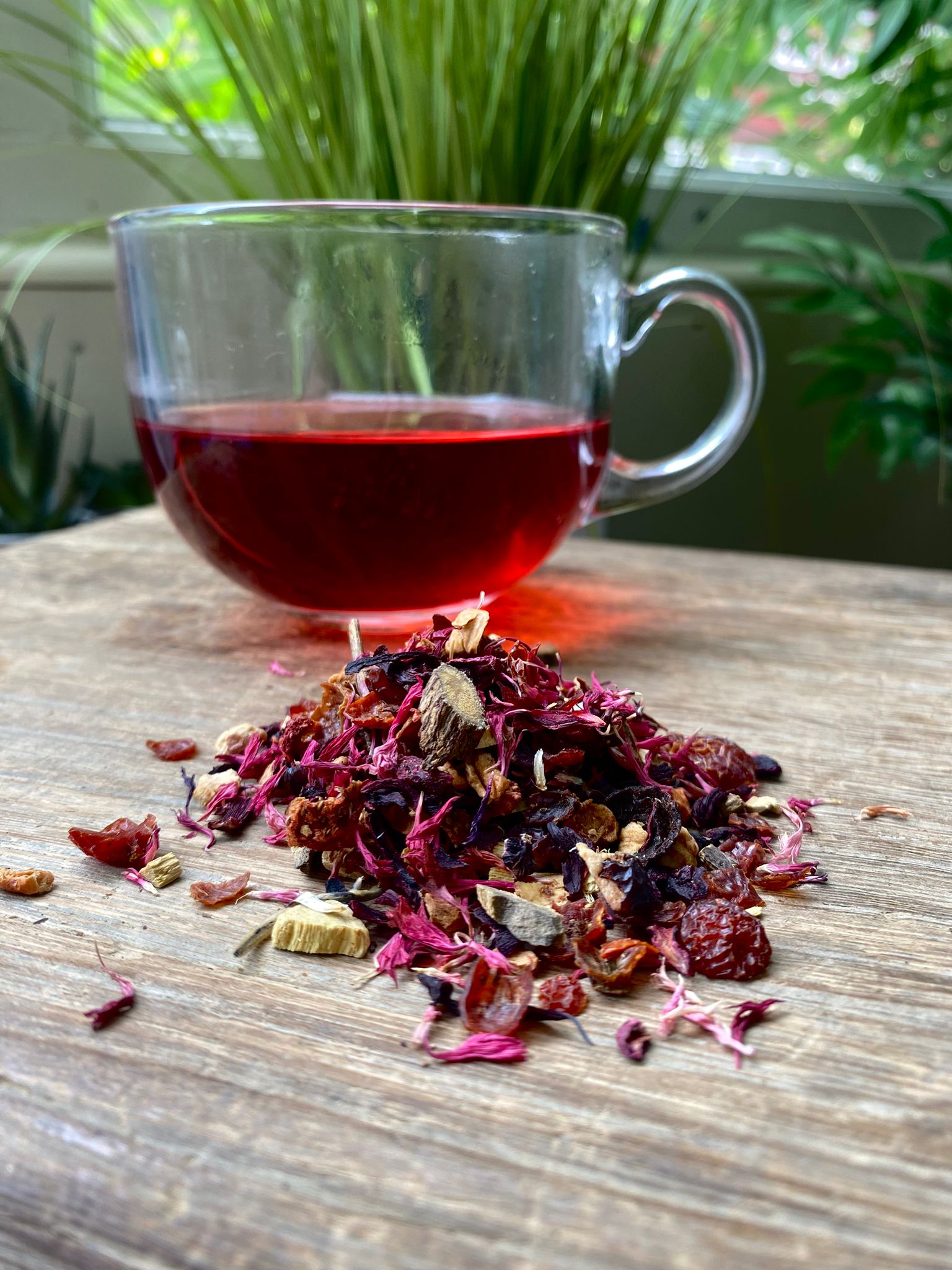 Marie’s strawberry laces loose leaf tea with brewed herbal tea in a clear glass mug and loose tea leaves on a wooden surface