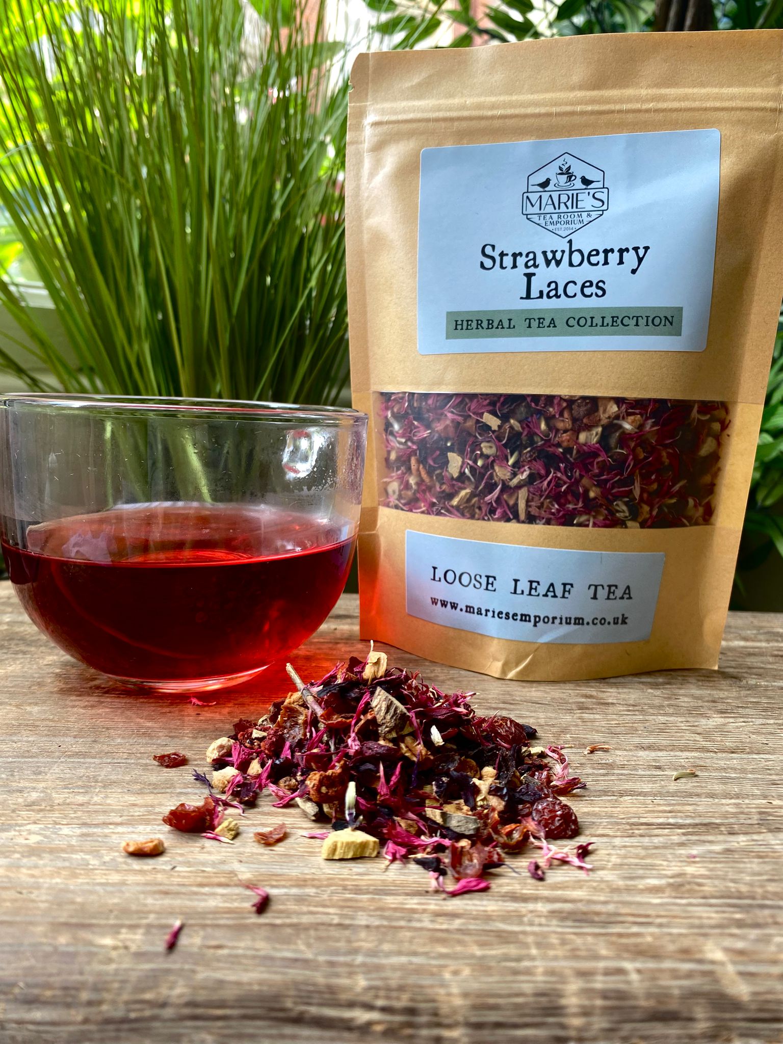 maries Strawberry Laces herbal tea package with a glass of tea on a wooden surface.