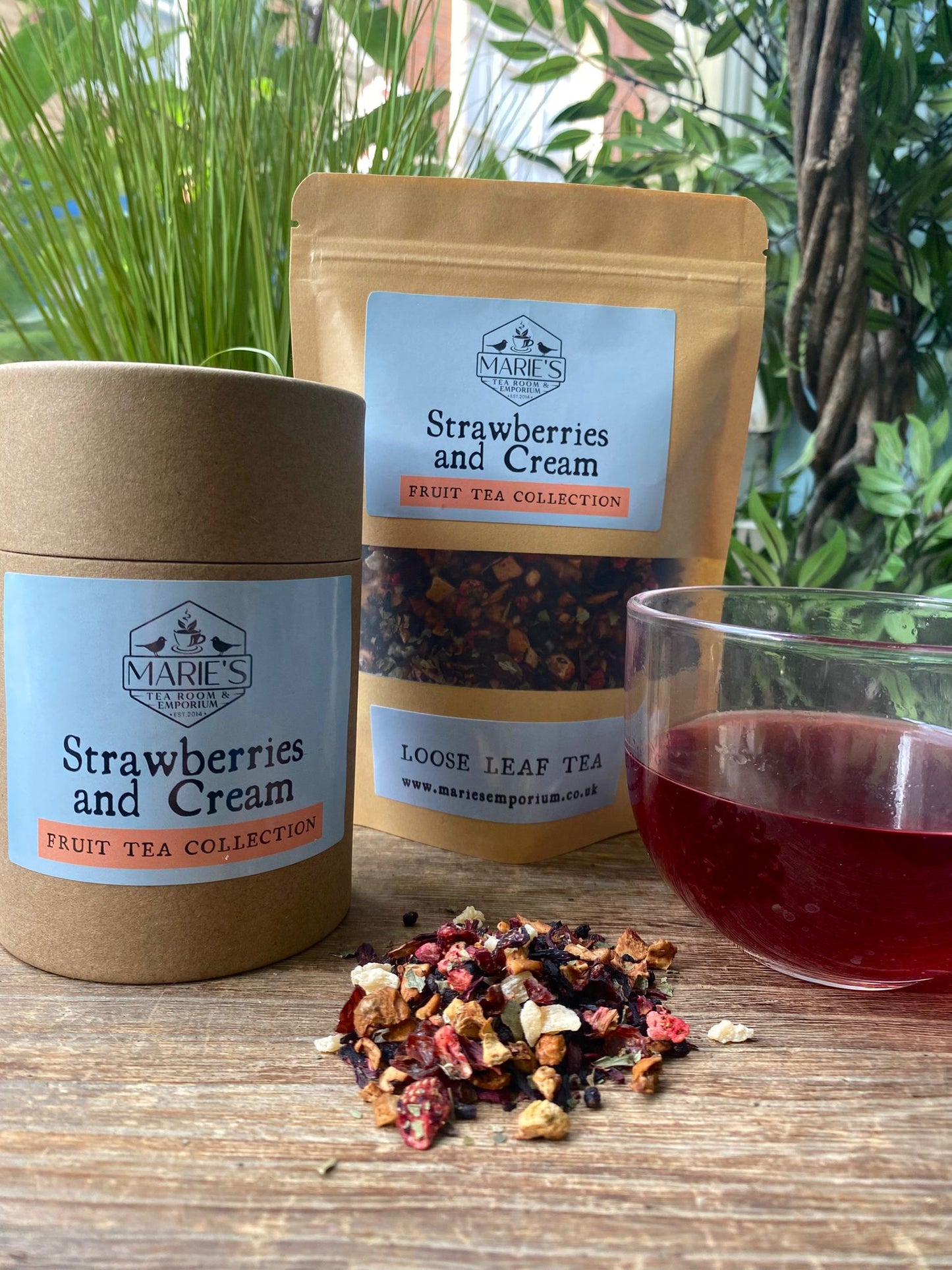 Marie's Tea Collection 'Strawberries and Cream' fruit tea set with loose leaf tea, jar, and glass of tea on a wooden surface.