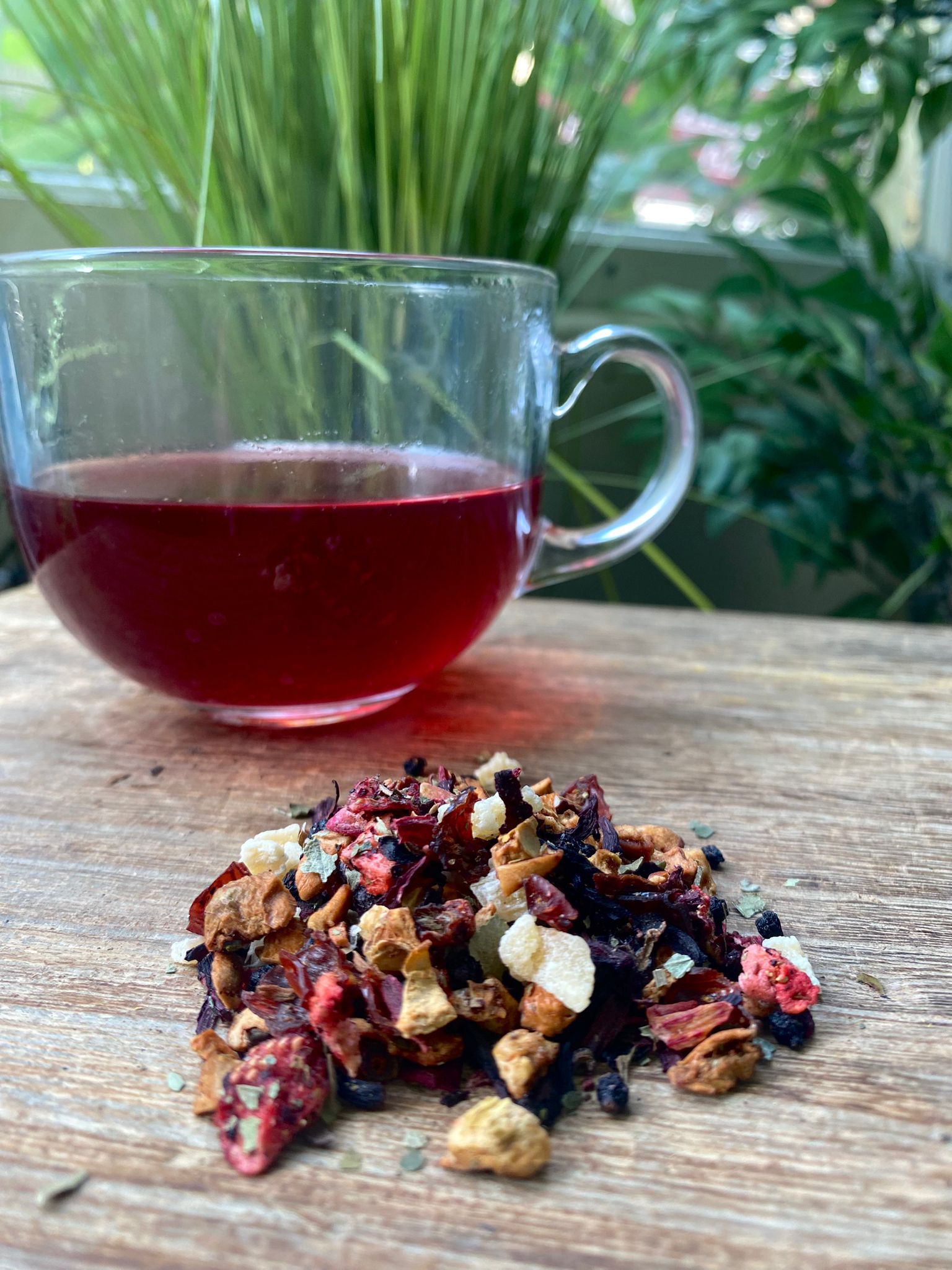 Maries Strawberries and Cream loose leaf tea with brewed fruit tea in a clear glass mug and loose tea leaves on a wooden surface
