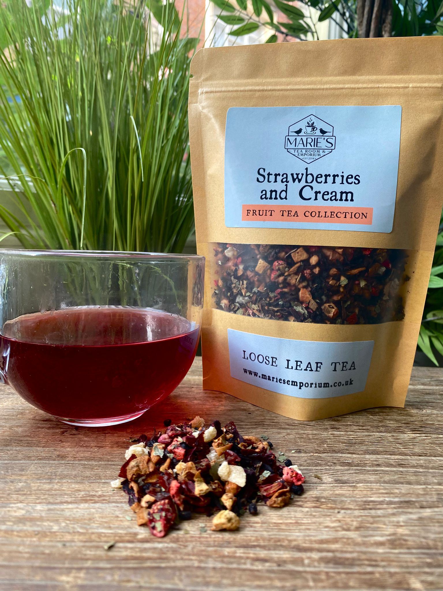 Tea packaging labeled 'Strawberries and Cream' with a glass of tea and loose tea leaves on a wooden surface.