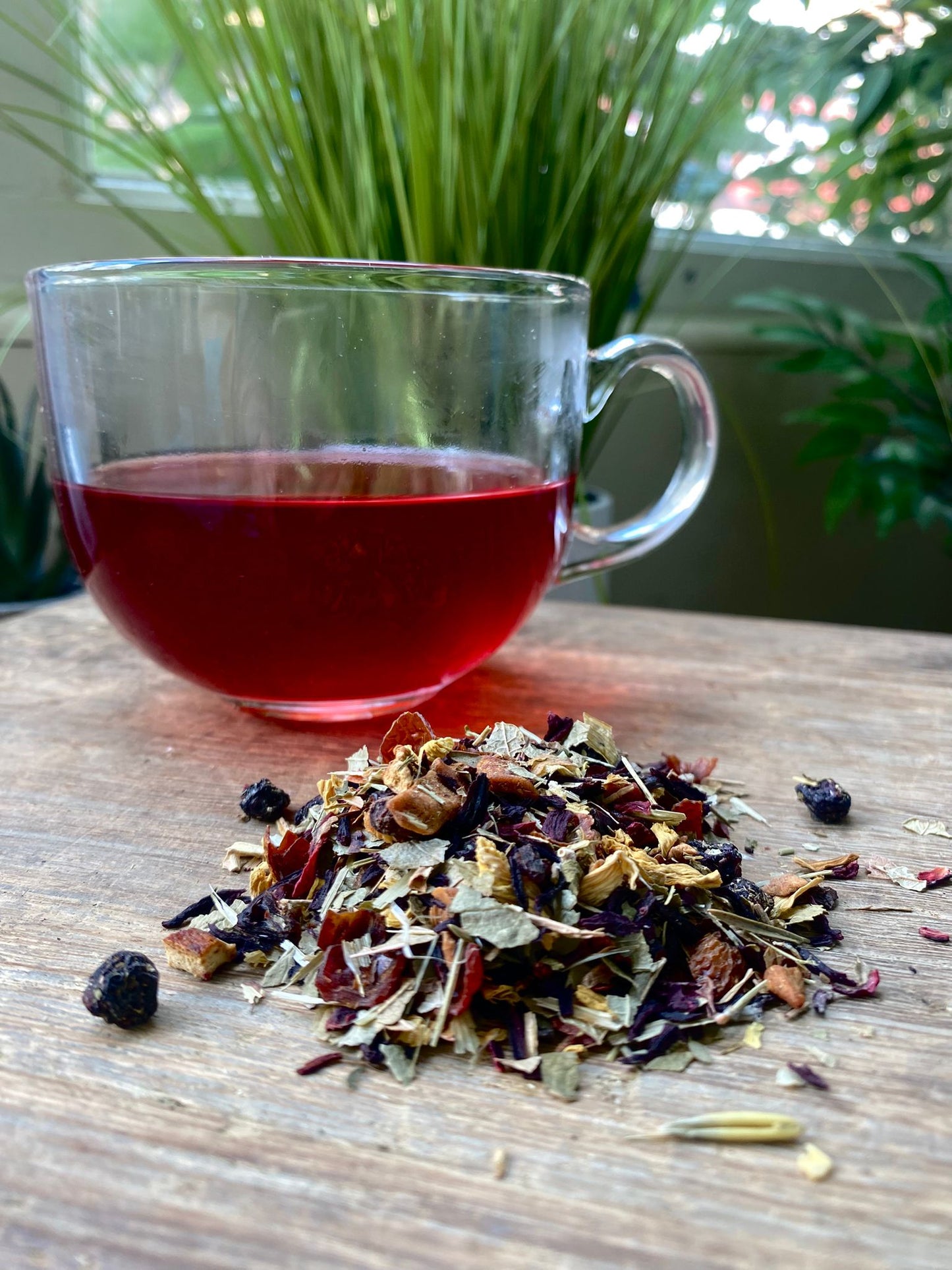 Maries The Woods of Virginia loose leaf tea with brewed fruit tea in a clear glass mug and loose tea leaves on a wooden surface