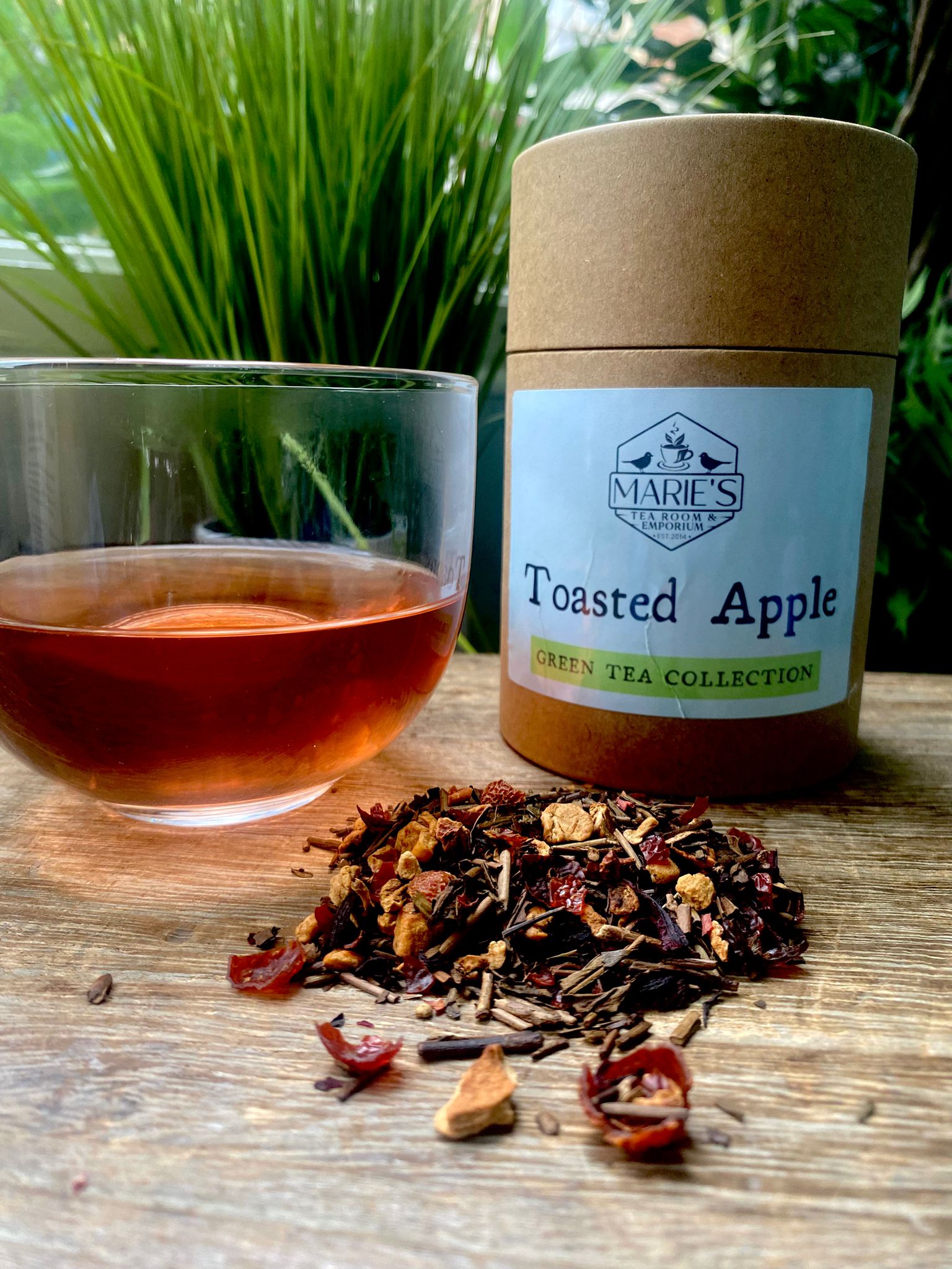 Marie's Toasted Apple loose leaf tea packaging with a glass of brewed tea and tea leaves on a wooden surface
