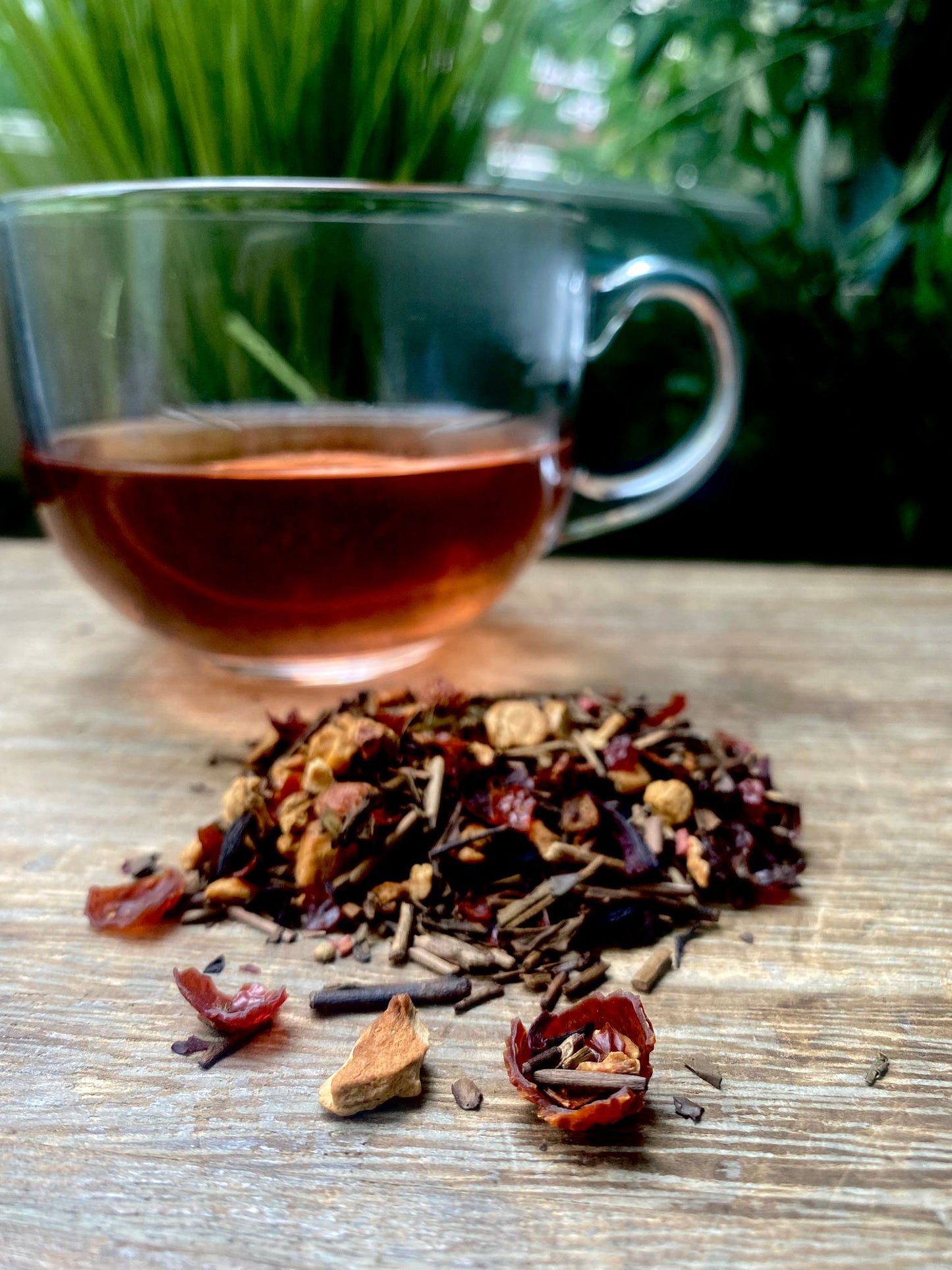 Toasted Apple loose leaf tea leaves and brewed tea in a glass on a wooden surface with greenery in the background