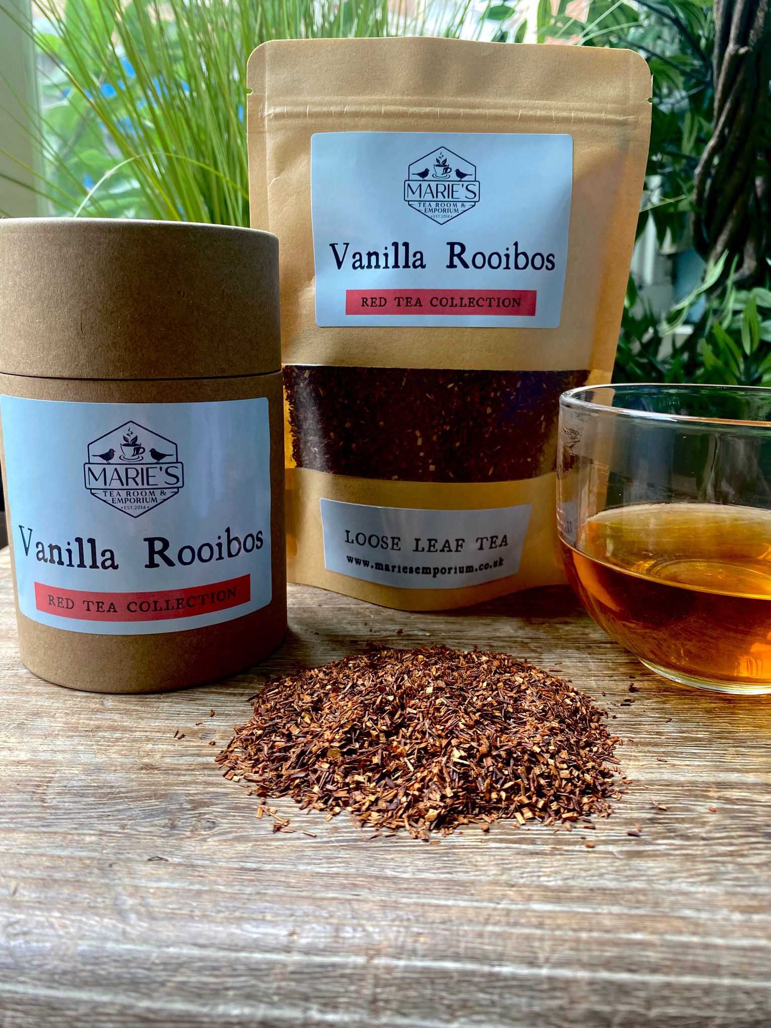 Marie's Vanilla Rooibos loose leaf tea packaging with a glass of tea on a wooden surface.