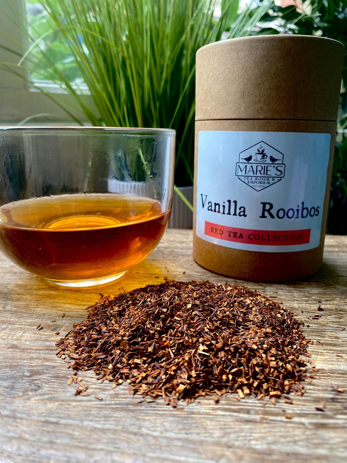 Vanilla Rooibos tea with a glass of tea and loose leaf tea leaves on a wooden surface.