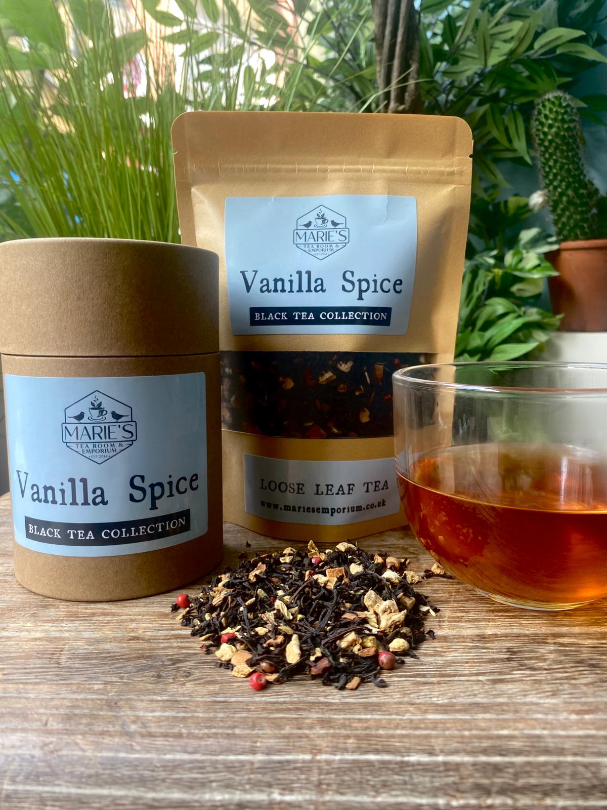 Vanilla Spice black tea maries collection with loose leaf tea, packaging, and a glass of tea on a wooden surface with plants in the background.