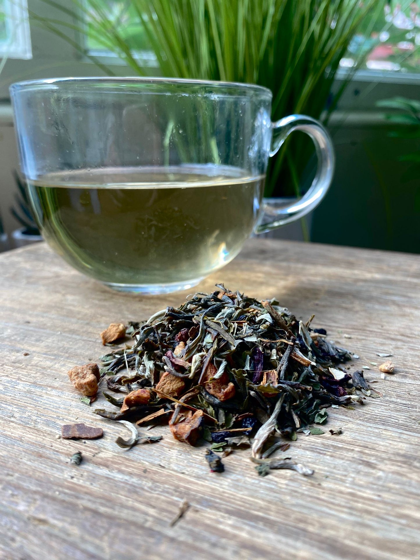 Marie's Emporium warming blackberry and mint tea with brewed White tea in a clear glass mug and loose leaf tea leaves on a wooden surface